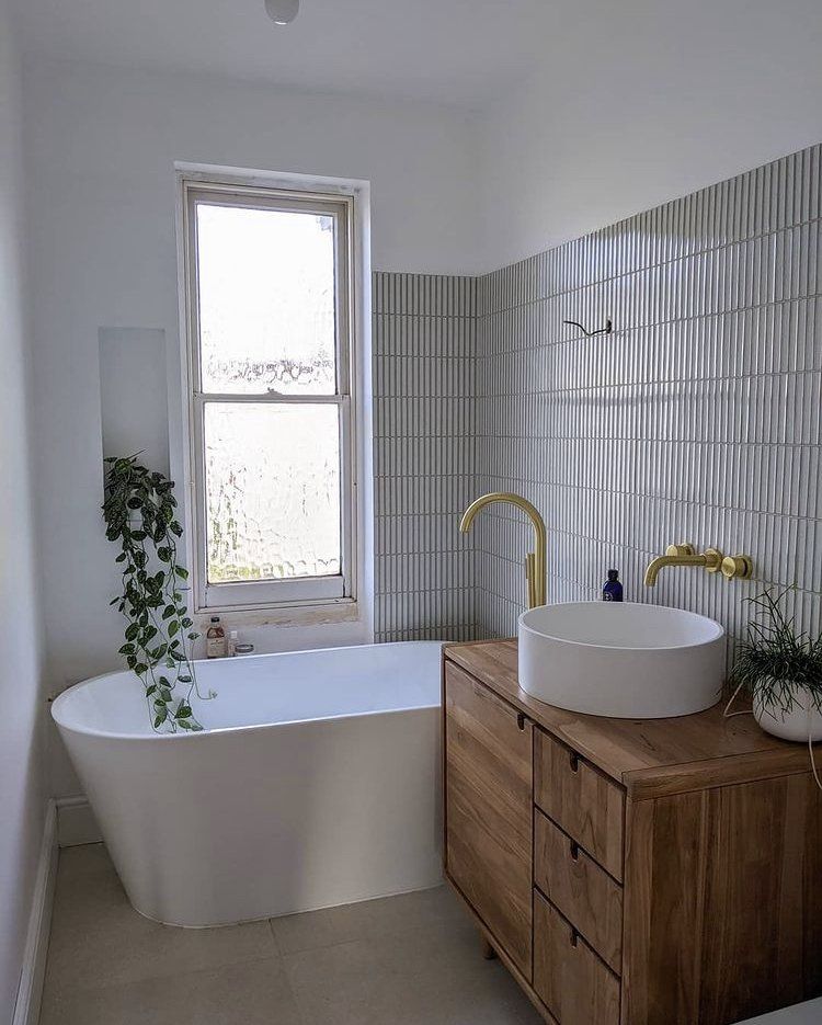 Modern bathroom with a freestanding tub, wood vanity, round sink, and a plant by the window.