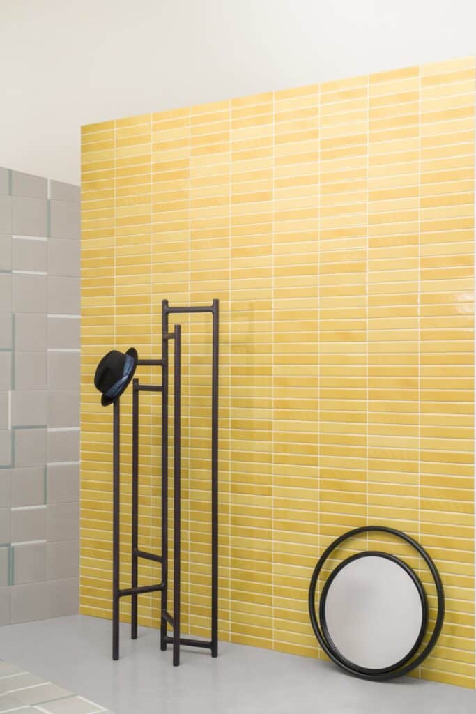 Yellow tiled wall with a black hat stand and a round mirror on the floor.