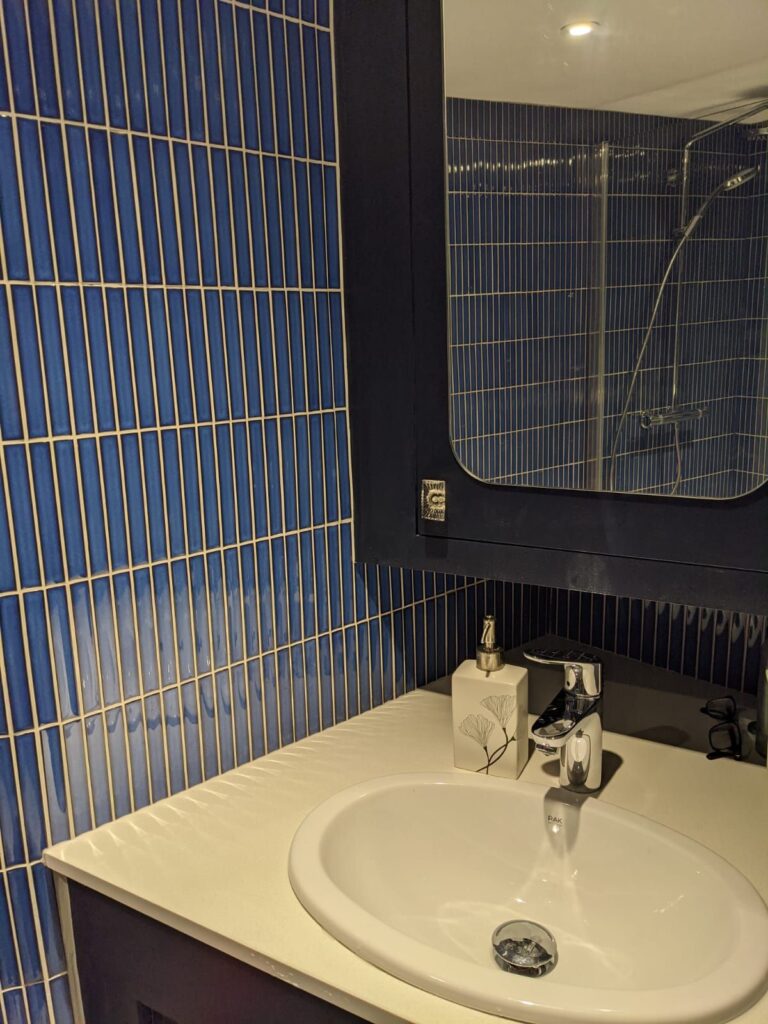 White bathroom sink with a faucet, mirror, and blue tiled wall. Soap dispenser on the counter.