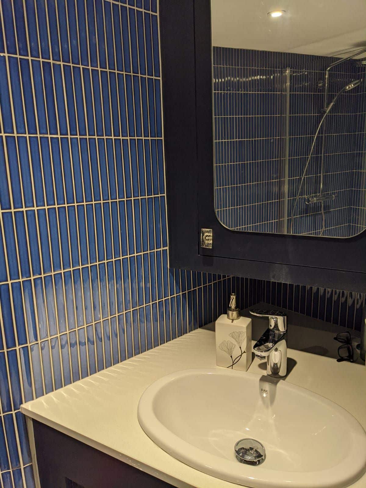 PHOTO-2020-12-27-20-11-38+2-1920w.jpg White bathroom sink with a faucet, mirror, and blue tiled wall. Soap dispenser on the counter.
