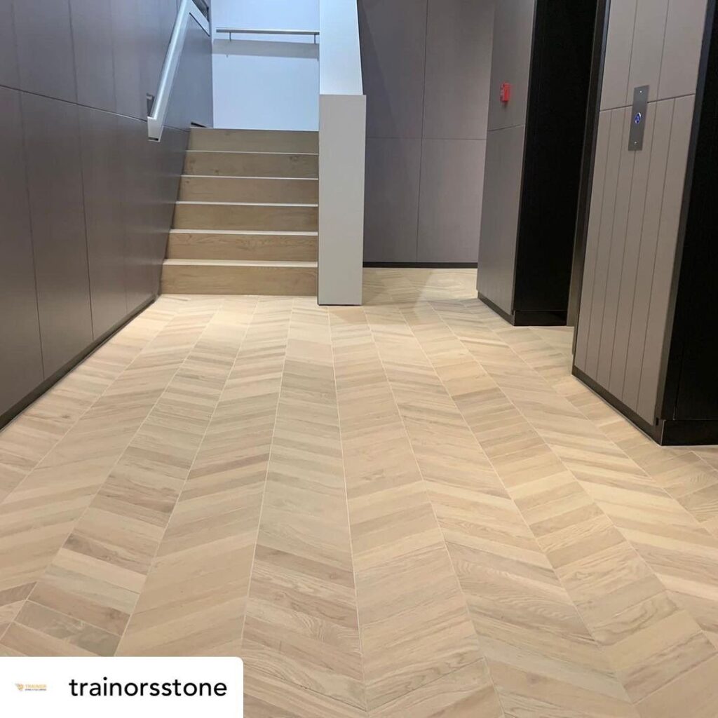 Light wood herringbone tile floor in a modern hallway near stairs and an elevator.