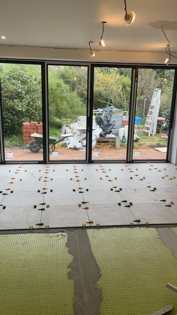 New tiles being installed in a room with large glass doors and a garden visible outside.