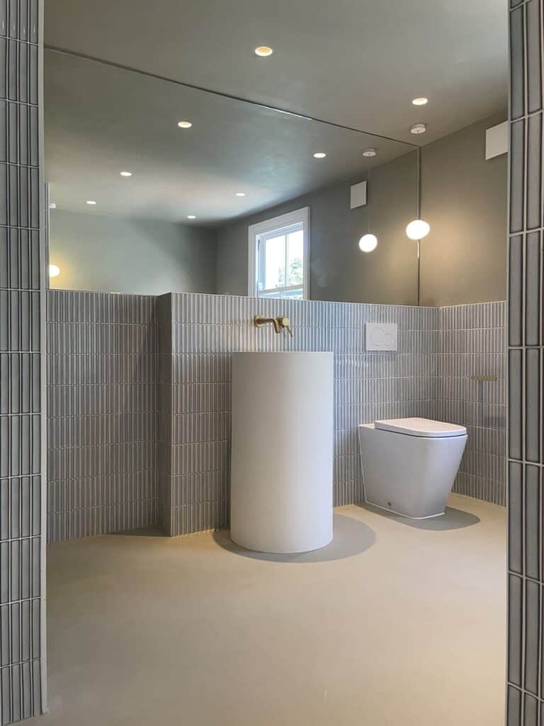 Photo+16-07-2022-+11+37+17-1920w.jpg Modern bathroom with a round white sink, toilet, and tiled walls under ceiling lights.