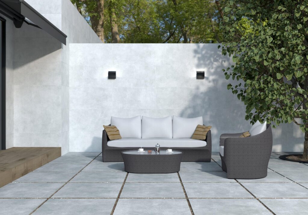 pam1900x2264-11bf5336-1920w.jpg Modern outdoor patio with a sofa, chair, and table on a tiled surface, next to a white wall and tree.