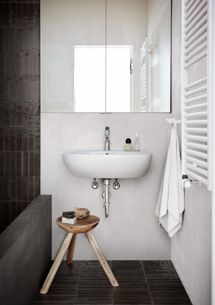 Marazzi_Crogiolo_Lume_003.jpg.1920x0_q75_crop-16173a15-1920w.jpg Modern bathroom with a white sink, mirrored cabinet, stool, and towel on a hook.