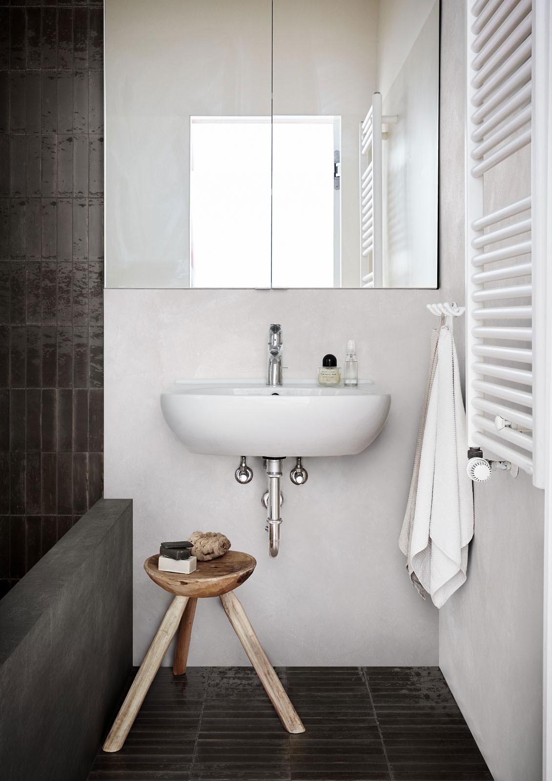 Modern bathroom with a white sink, mirrored cabinet, stool, and towel on a hook.