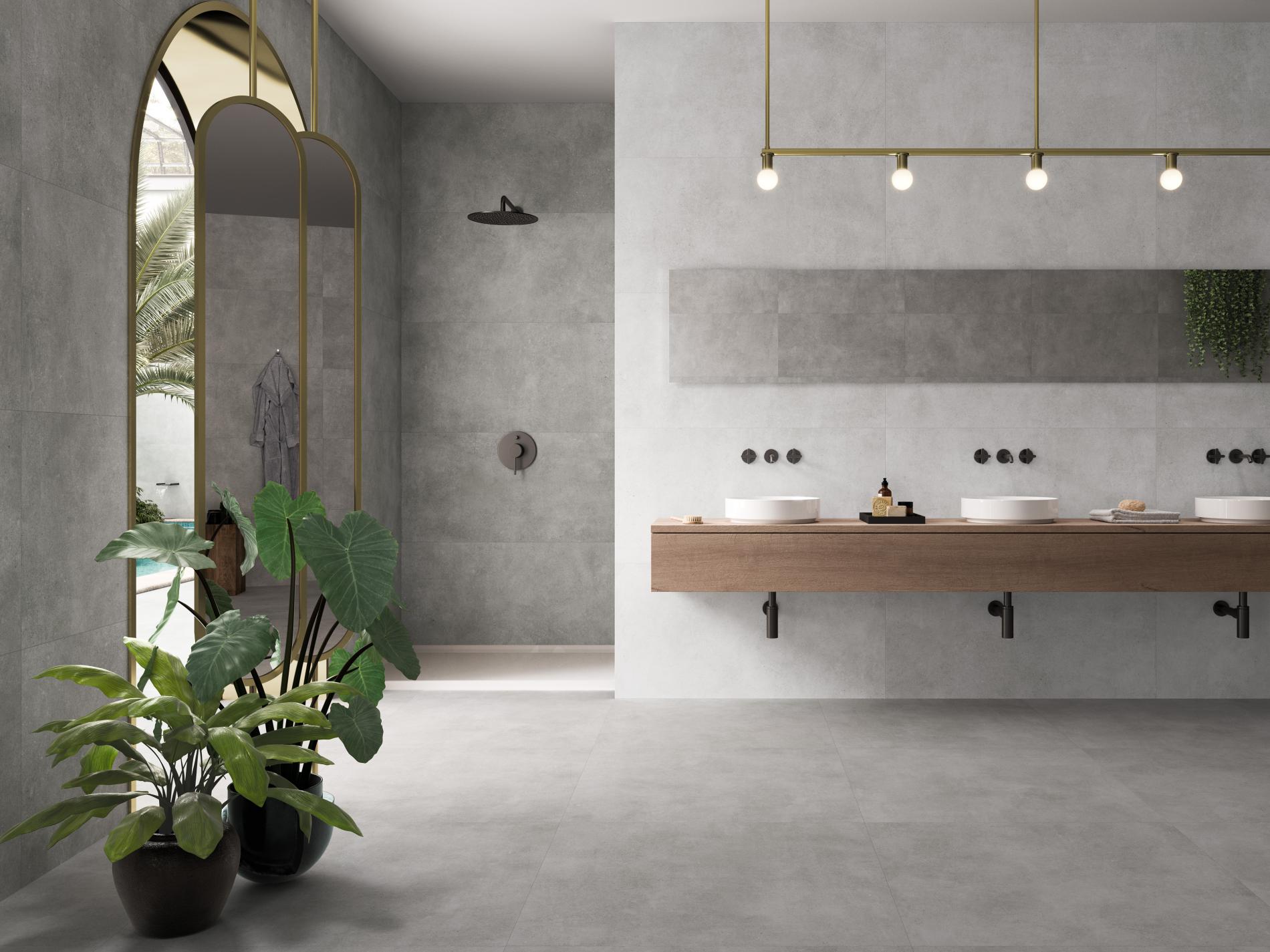 Modern bathroom with gray walls, large mirror, double sinks, and potted plants near a tall arched window.