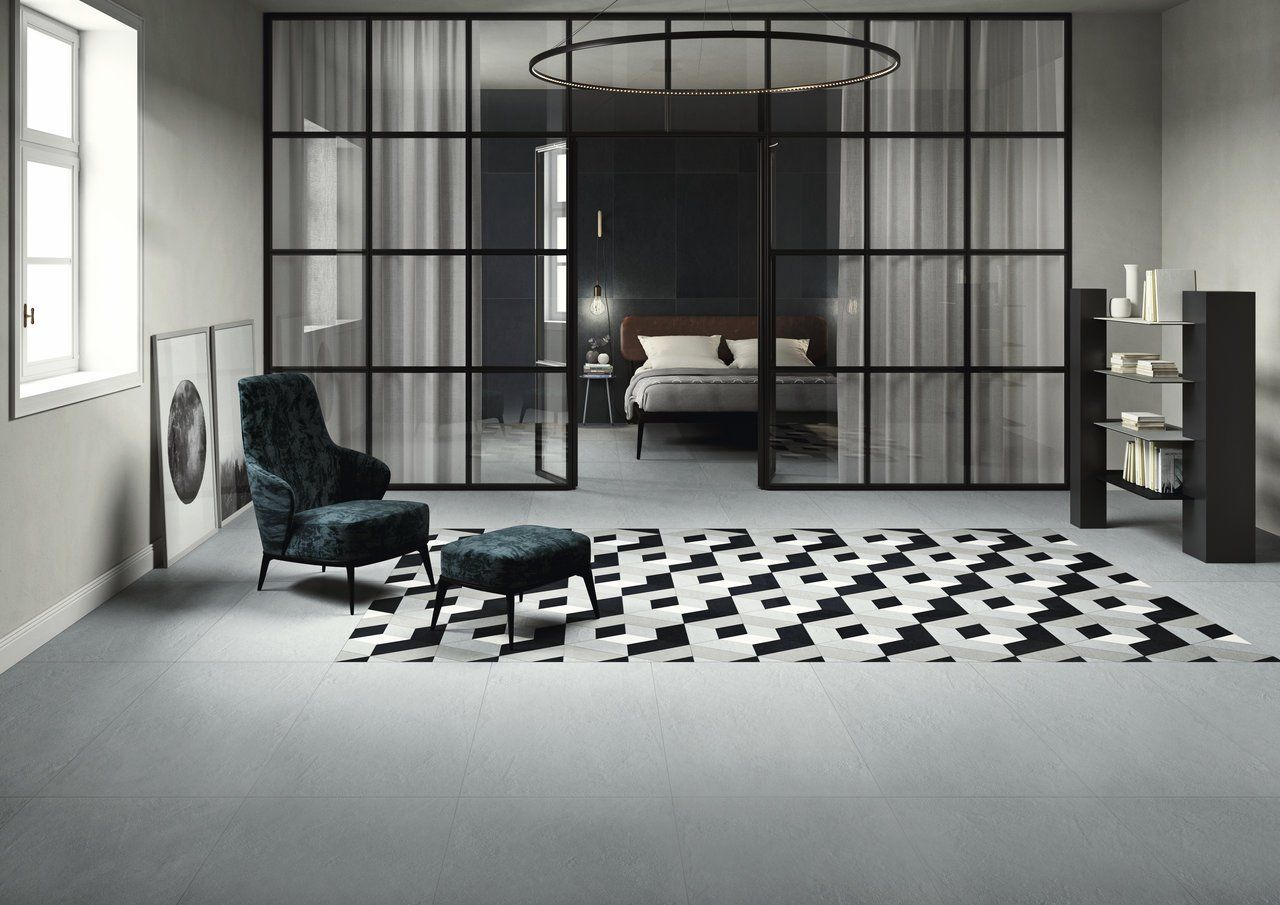 Naples+Pattern+Floor+Tiles+Bedroom+-1920w.jpg Modern bedroom with glass walls, patterned rug, dark chair, and shelf in a minimalist setting.