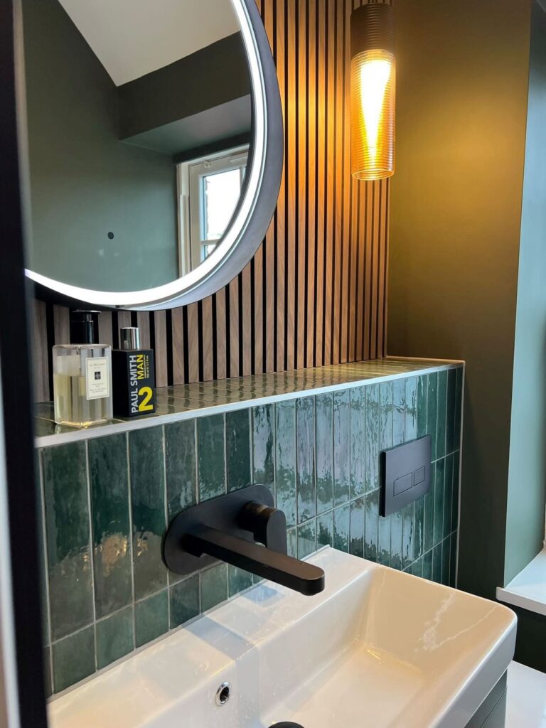 Modern bathroom with green tiles, a white sink, round mirror, and a wall sconce light fixture.