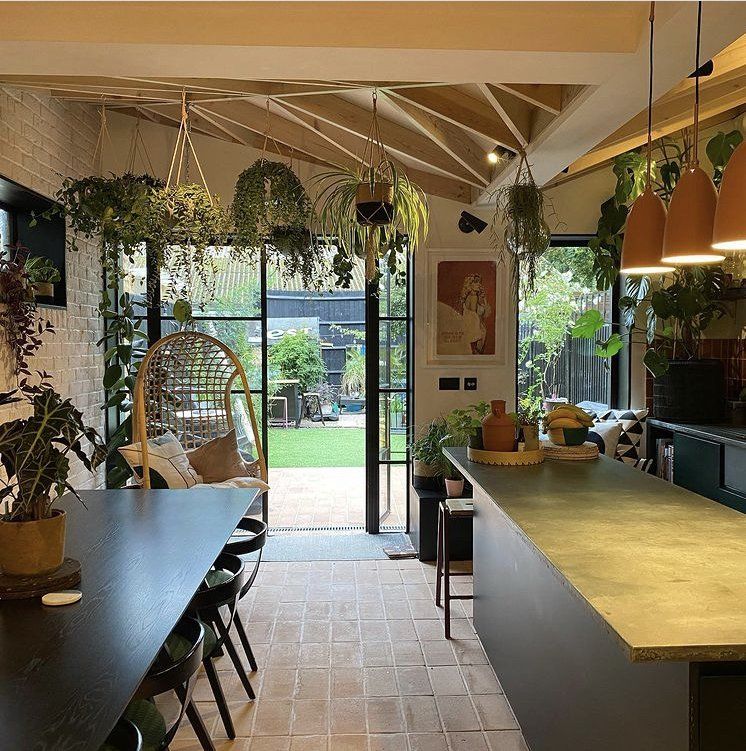 Modern kitchen with terracotta tile floor, hanging plants, and large windows opening to a garden.