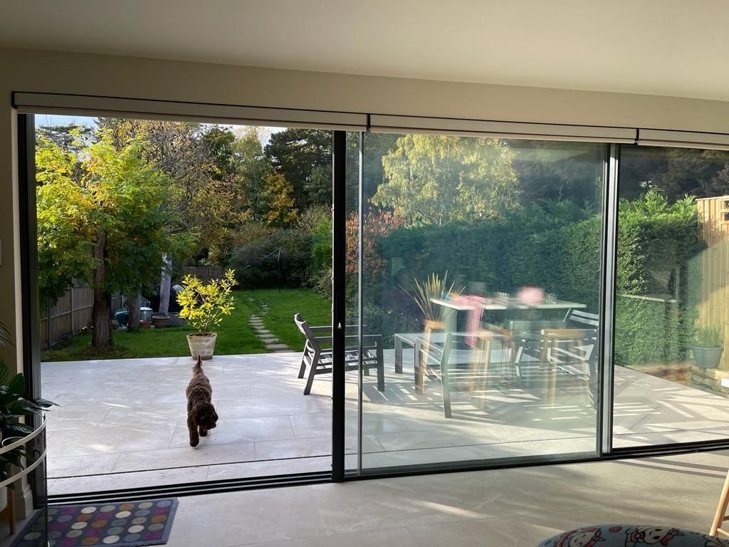 A dog runs outside through sliding glass doors to a patio and a green backyard.