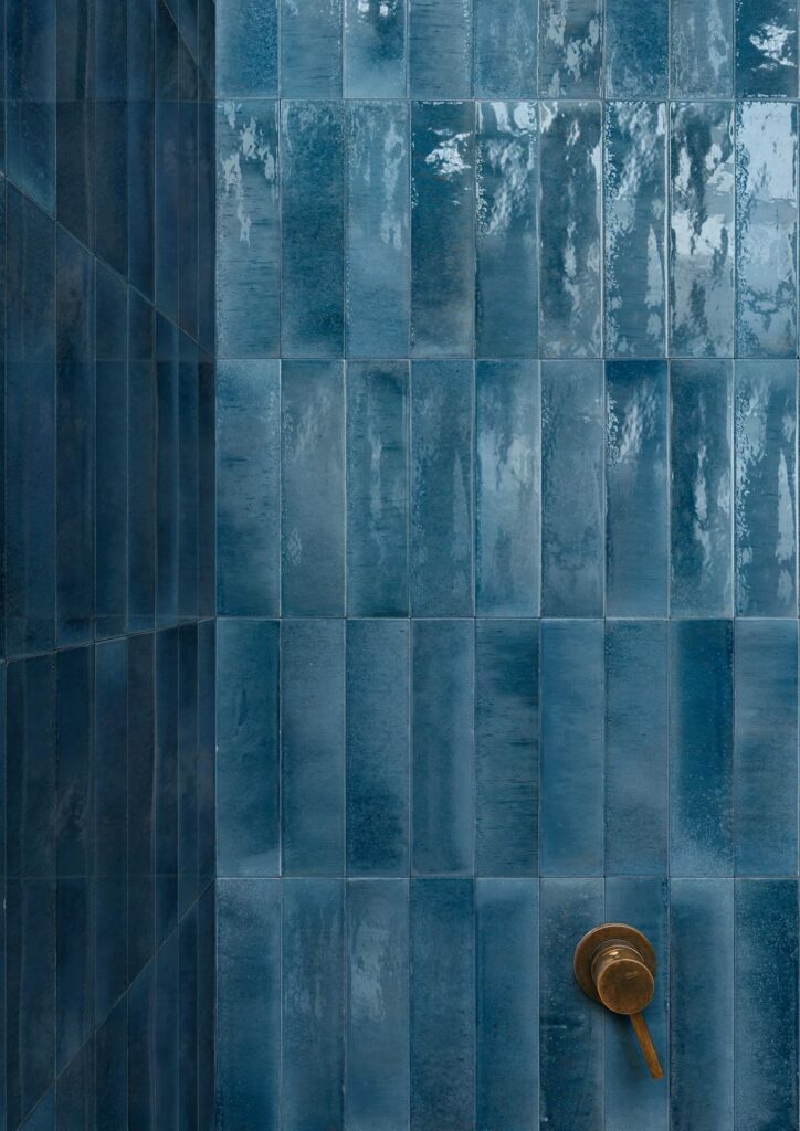Blue rectangular tiles cover a shower wall with a bronze shower handle visible.