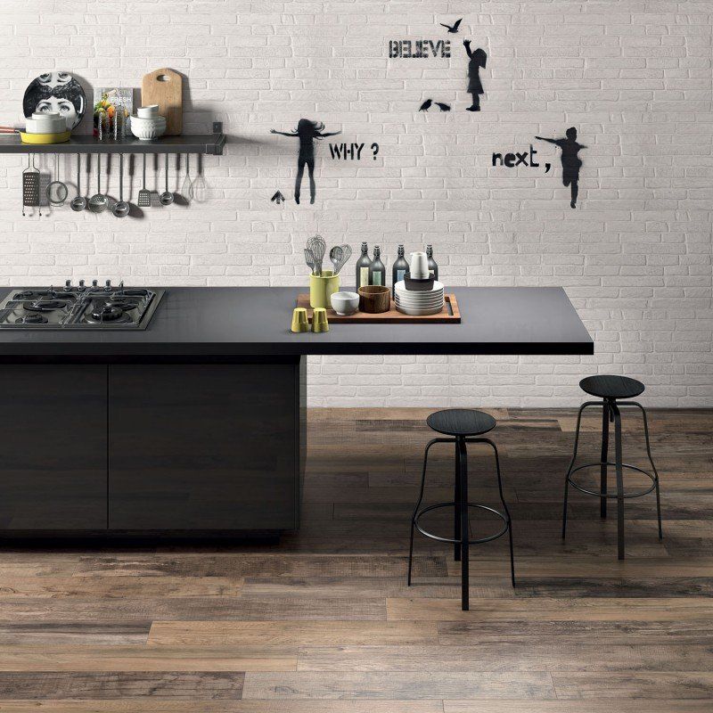1-93166c1f-1920w.jpg Modern kitchen with a black island, two stools, wall art, and cooking utensils on a shelf.