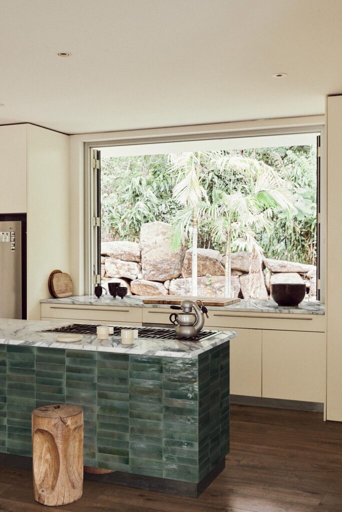 Modern kitchen with a green-tiled island, a large window, and a view of rocks and greenery outside.
