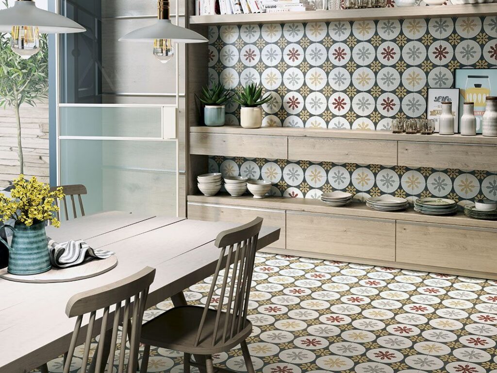 1-05f4e90c-1920w.jpg Kitchen with patterned tile floor and backsplash, wooden table, and open shelves with dishes and plants.