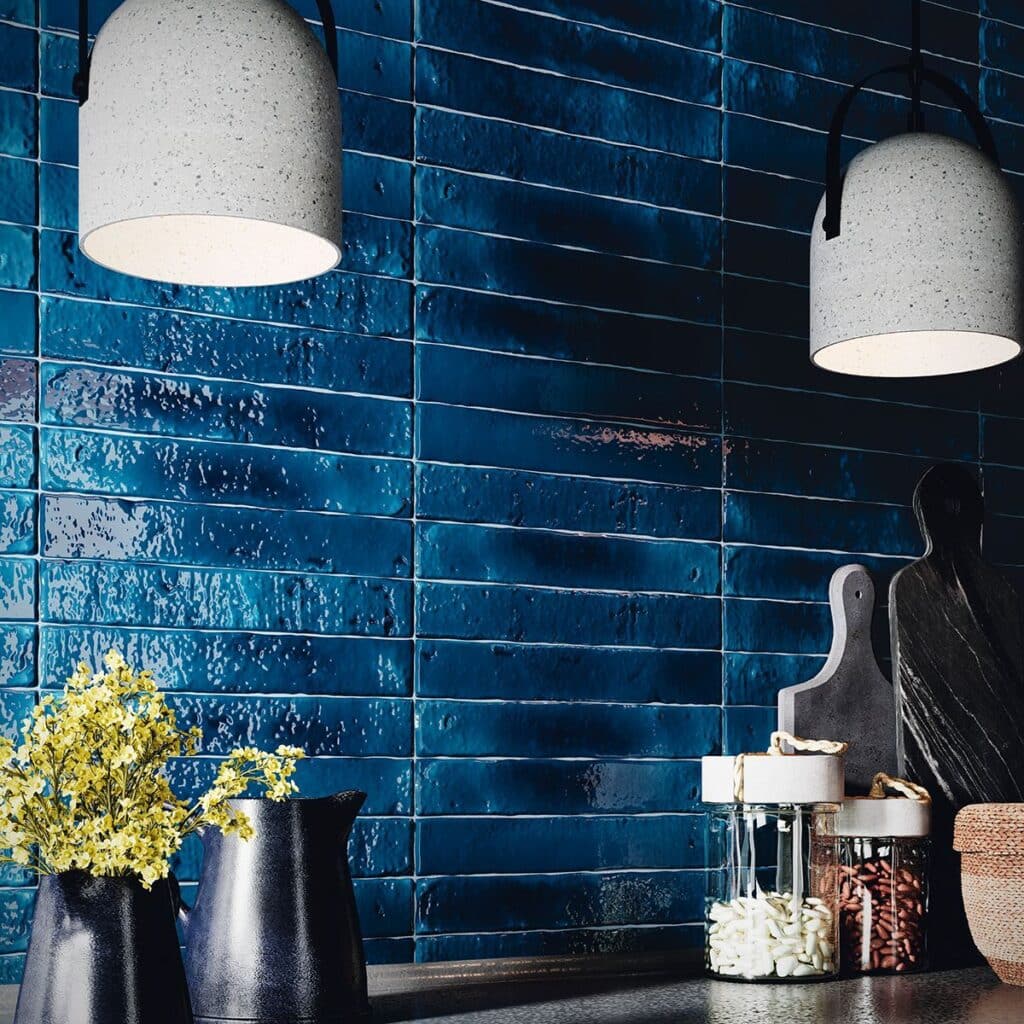 Two hanging lights above a dark countertop with blue tiled backsplash and kitchen accessories.