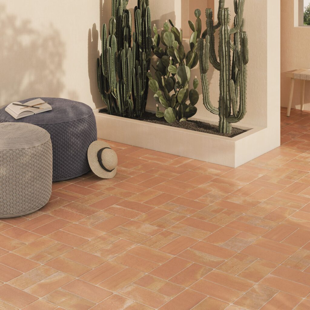 Terracotta tile floor with round poufs, a hat, and tall cacti against a beige wall.