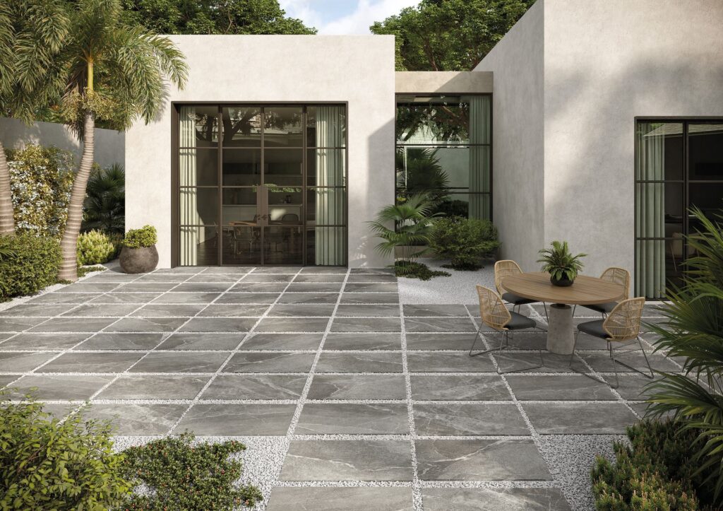 Modern patio with large gray tiles, outdoor furniture, and surrounding greenery.