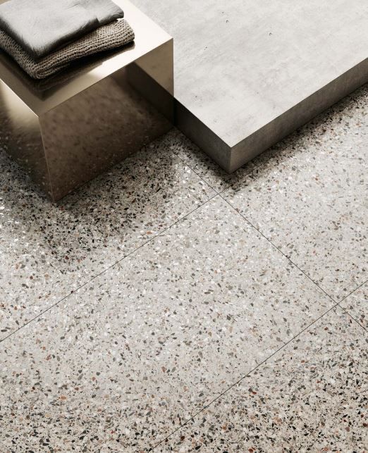 Gray terrazzo tile floor with a bench and folded towels in a modern, minimalist space.