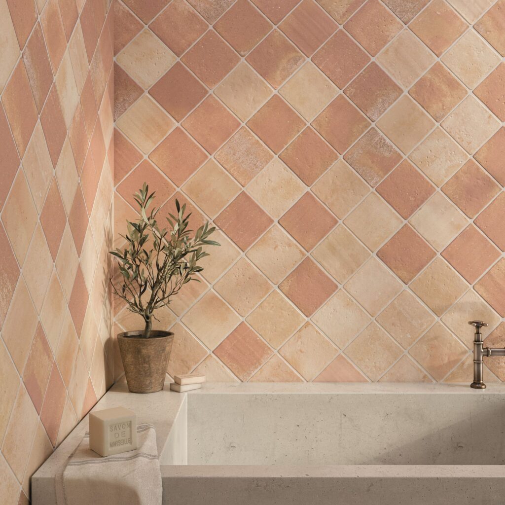 Peach and cream square tiles on bathroom wall, with a potted plant and bathtub in the corner.