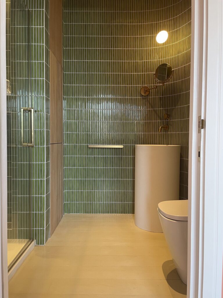 Modern bathroom with green tiled shower, round basin, and wall-mounted toilet.