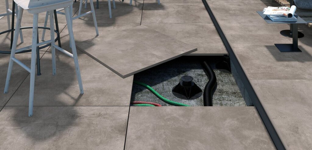 A floor tile is lifted to show cables and pipes underneath an outdoor patio area.