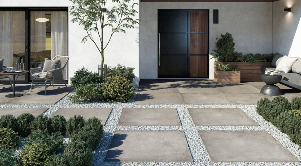 Modern patio with square stone pavers, greenery, and outdoor seating by a house entrance.