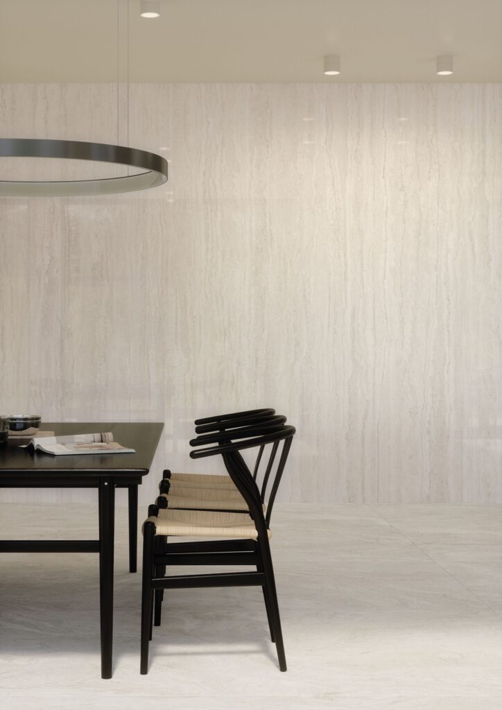 Minimalist dining area with black chairs and table, light stone wall and floor, and modern lighting.