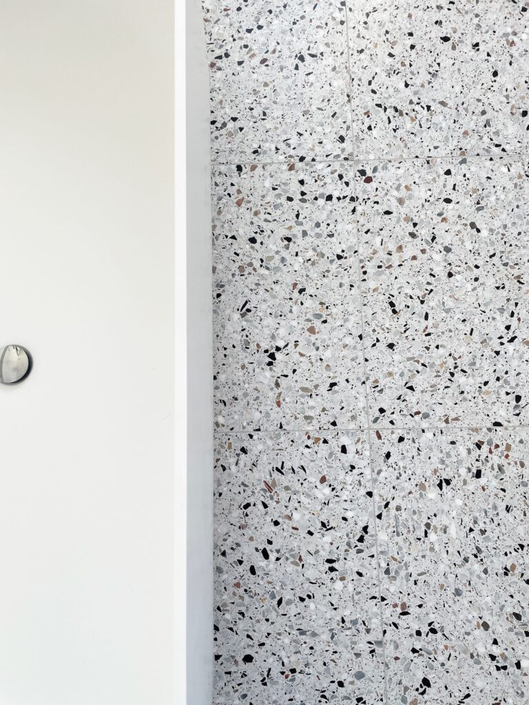 White bathroom wall next to a terrazzo wall with speckled black and gray patterns.
