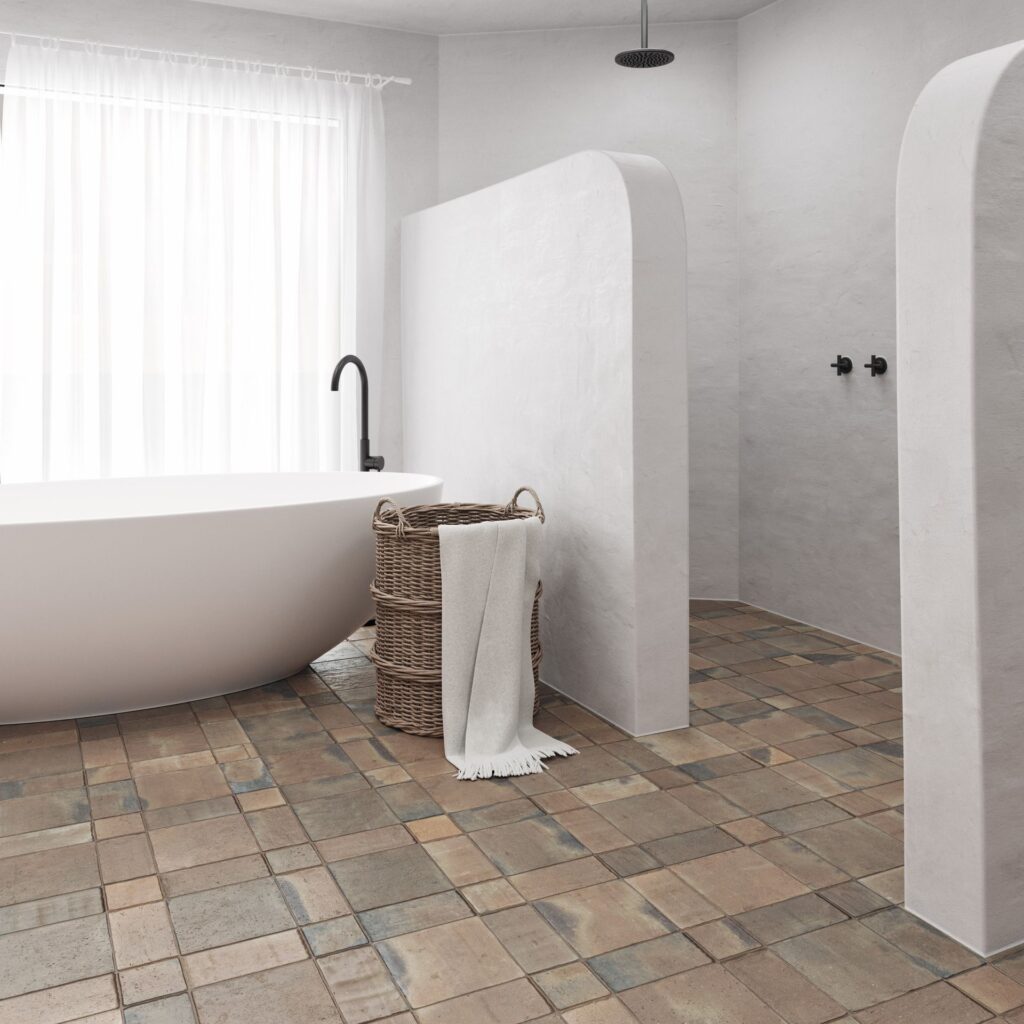 Modern bathroom with a freestanding tub, woven basket, and rustic tiled floor.