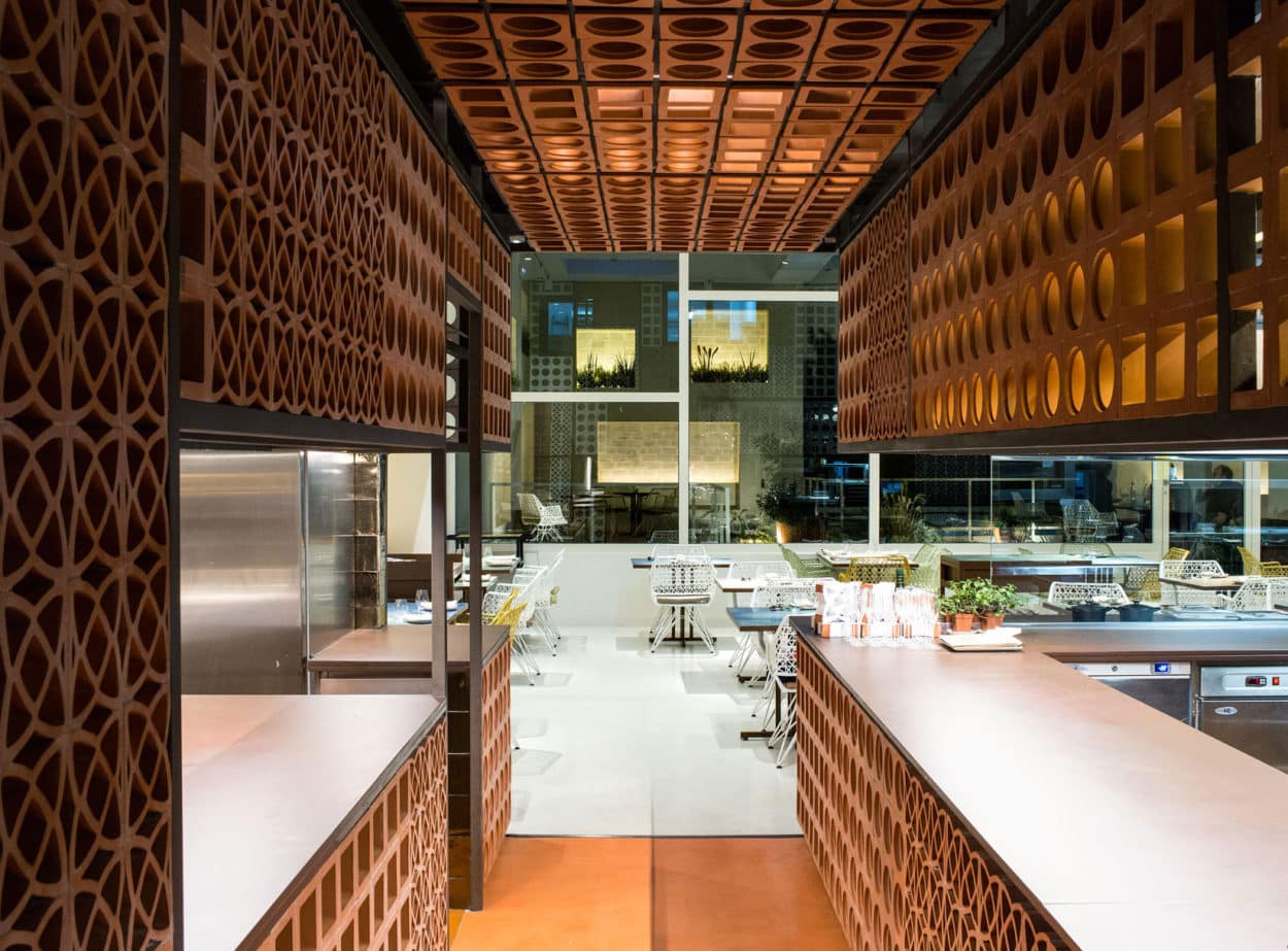 Modern kitchen with geometric terracotta tiles and a view of a bright dining area with white chairs.