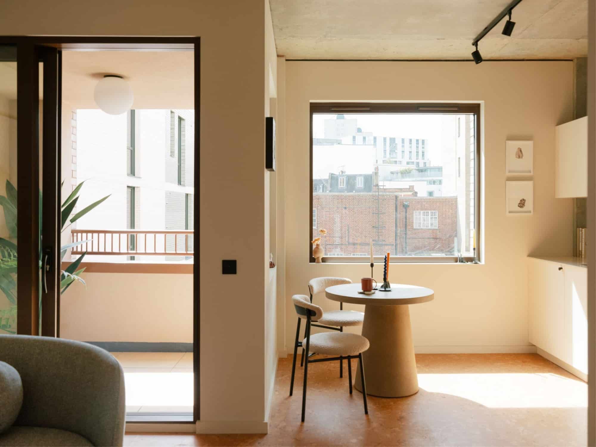 Modern dining area with round table, two chairs, and large window letting in natural light.