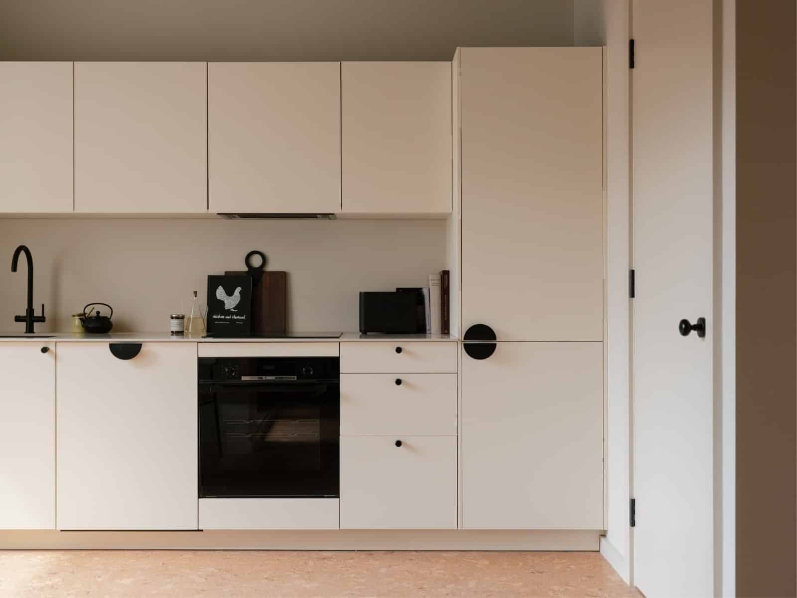 Minimalist kitchen with cream cabinets, black handles, and modern fixtures.