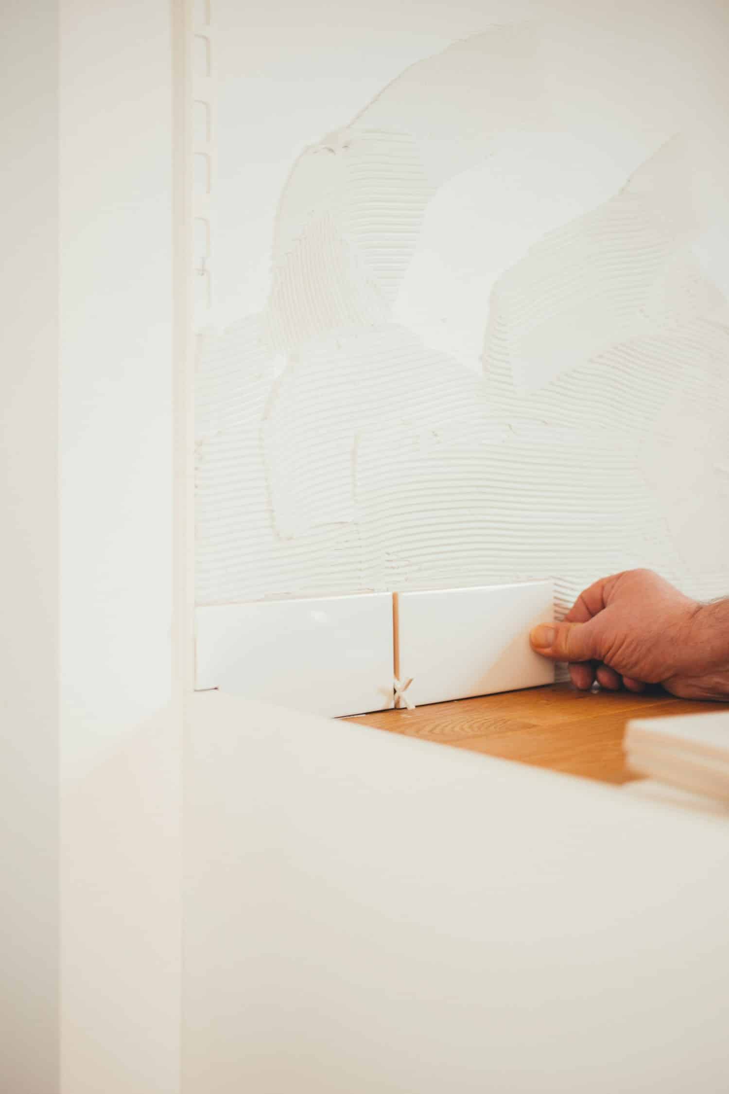 A hand places white tiles on a wall with adhesive, preparing for tile installation.