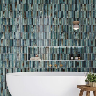 Modern bathroom with blue-green vertical tile wall, white tub, and wooden side table with a plant.