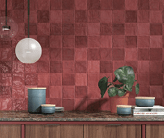 Red tile backsplash with a potted plant, bowls, and hanging lights on a kitchen counter.