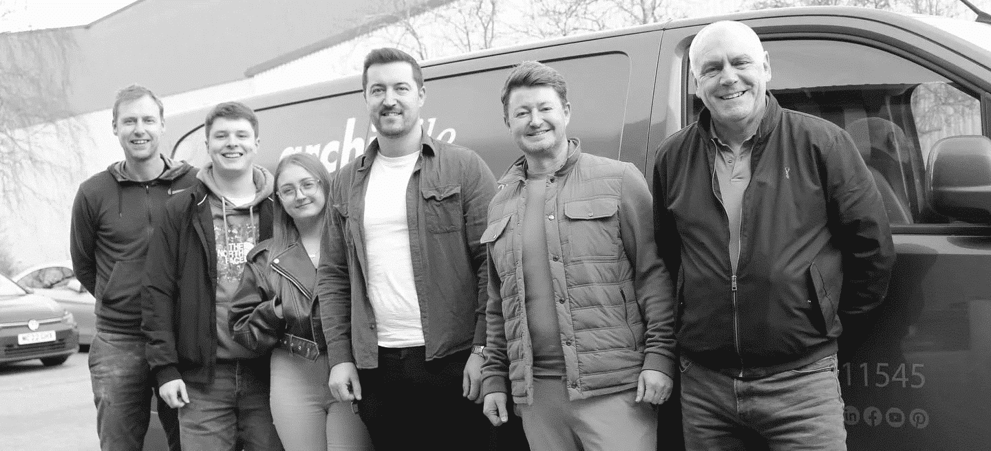Six people stand smiling in front of a van, posing for a group photo.