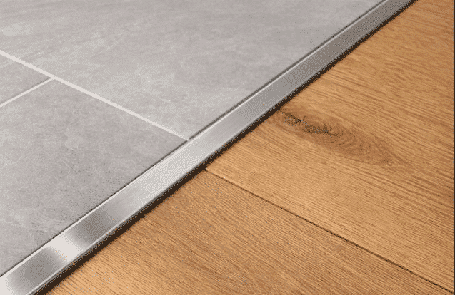 Gray tile floor meets wood flooring with a metal trim transition strip.