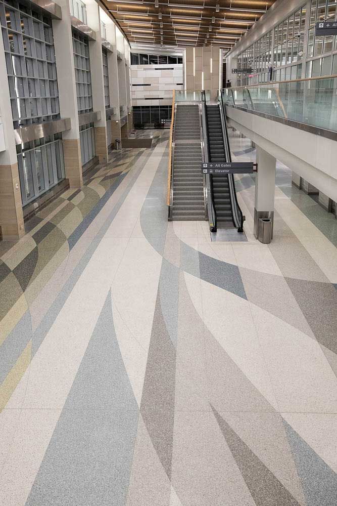 Williston+Basin+International+Airport-1920w.jpg Modern airport interior with escalators, glass railings, and patterned flooring.