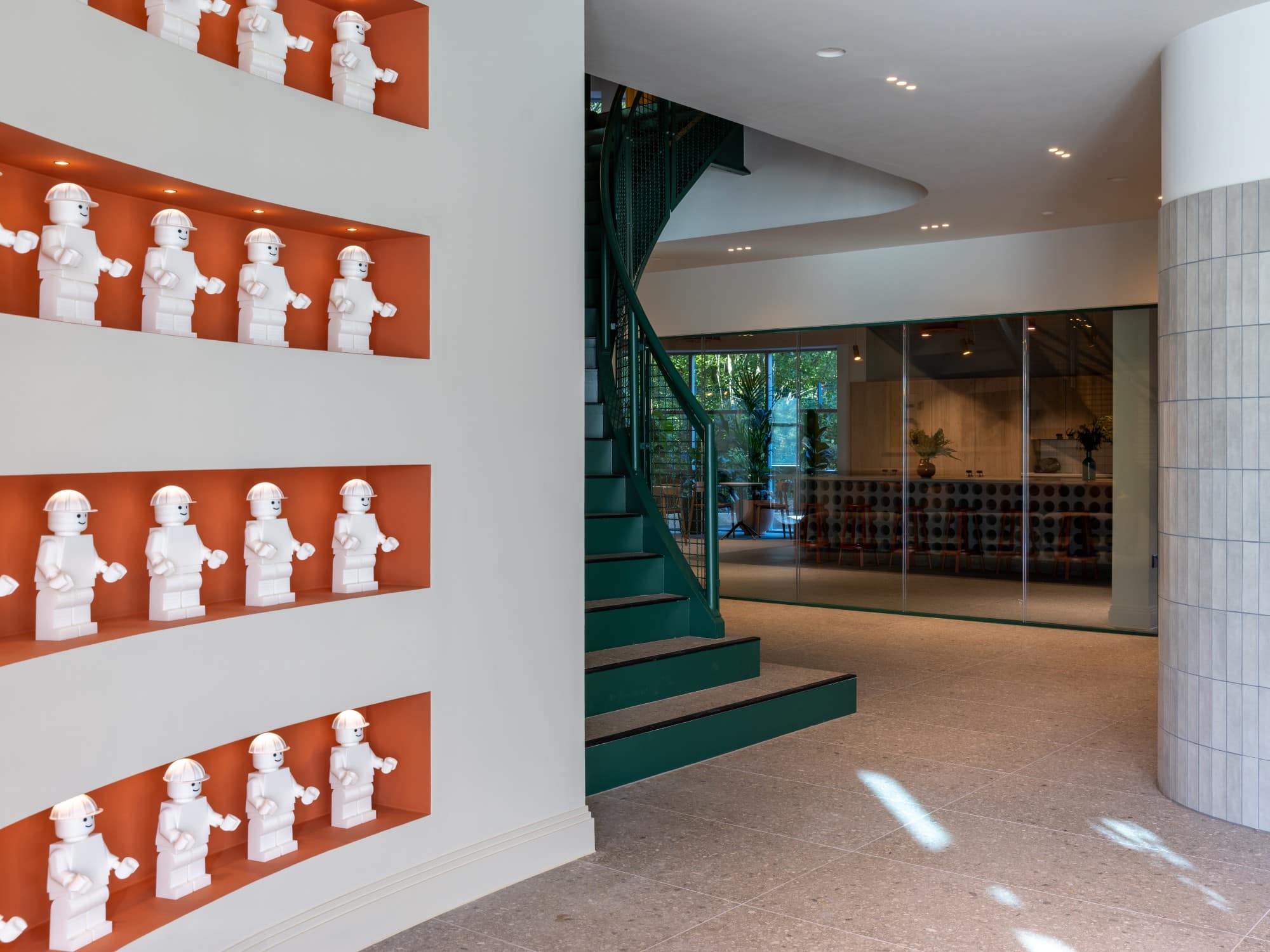 Display shelves with white busts on a wall next to a green spiral staircase in a modern interior.