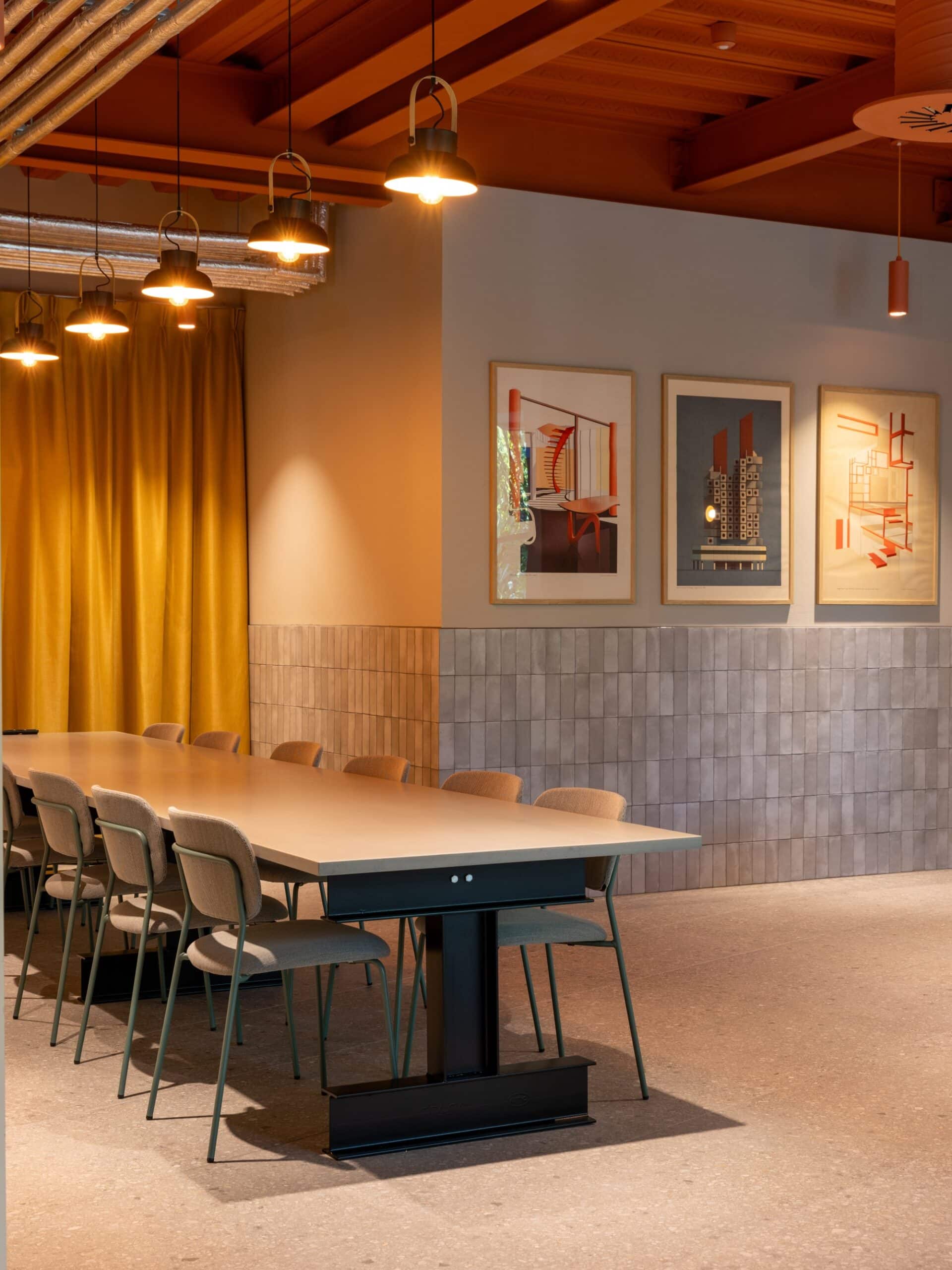 Modern meeting room with a long table, chairs, yellow curtains, and framed art on the wall.
