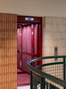 A red elevator with open doors on the first floor in a building hallway.