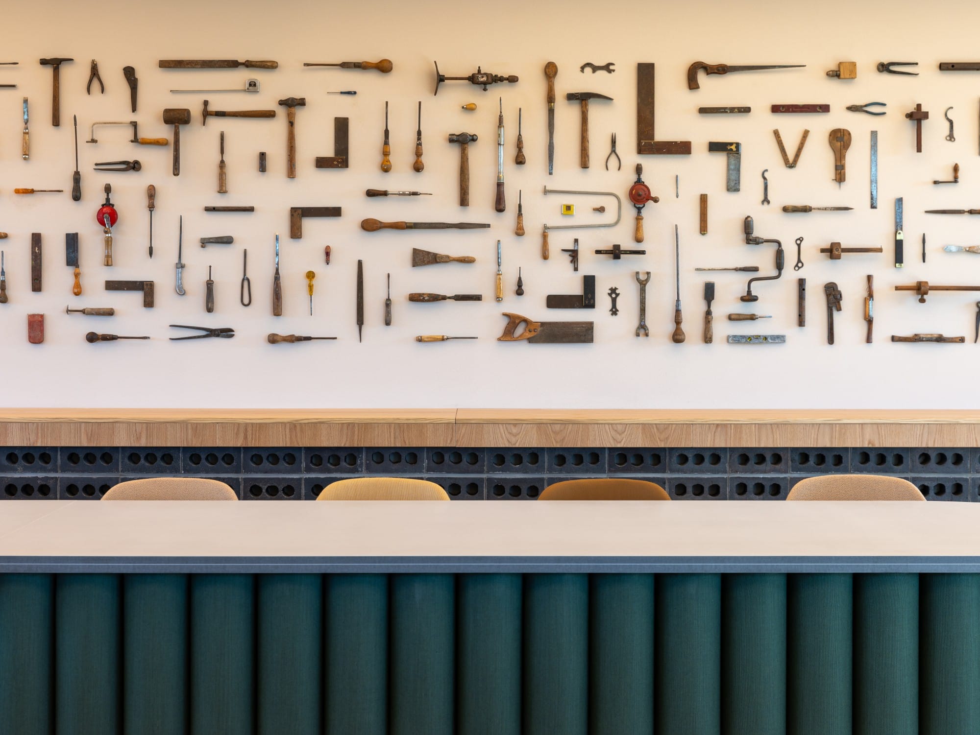 A wall display of vintage tools above a row of chairs and a counter.