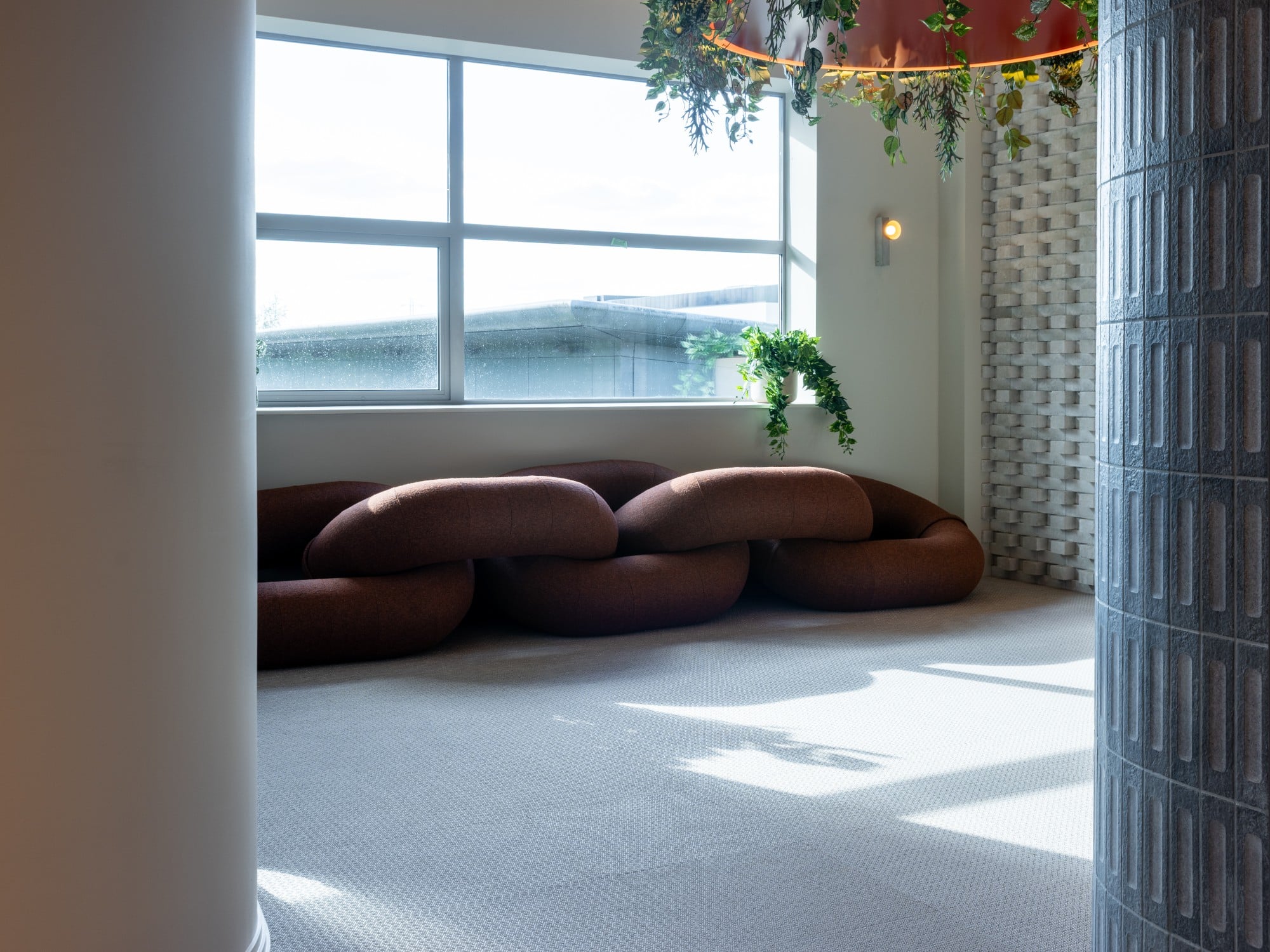Brown modern sofa in a bright room with large windows and indoor plants.