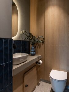 Modern bathroom with a vessel sink, toilet, blue tiles, wood walls, and a vase with greenery.