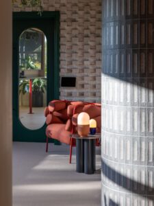 A modern living room with a red sofa, side table, two lamps, and a green door in the background.