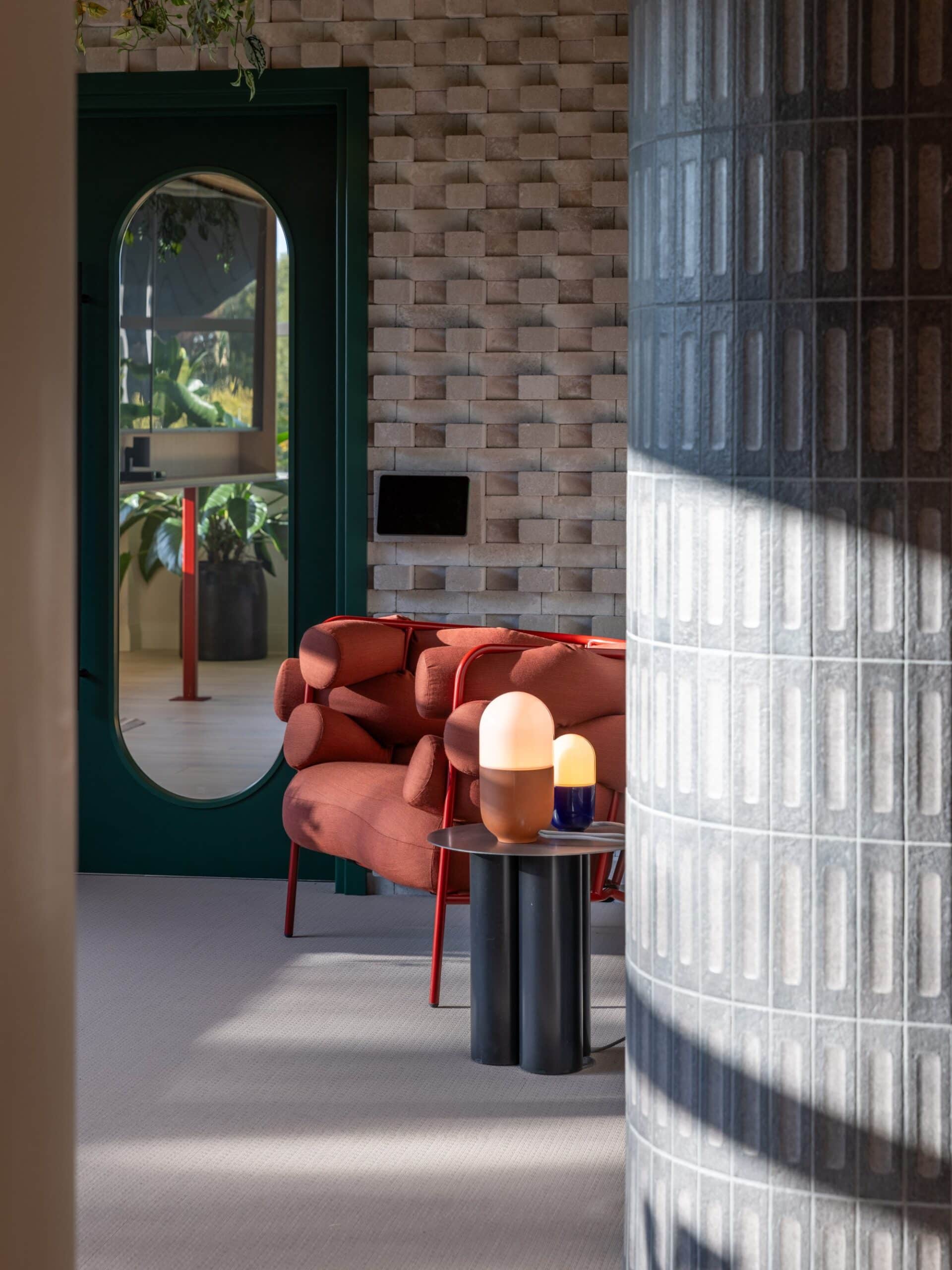 A modern living room with a red sofa, side table, two lamps, and a green door in the background.