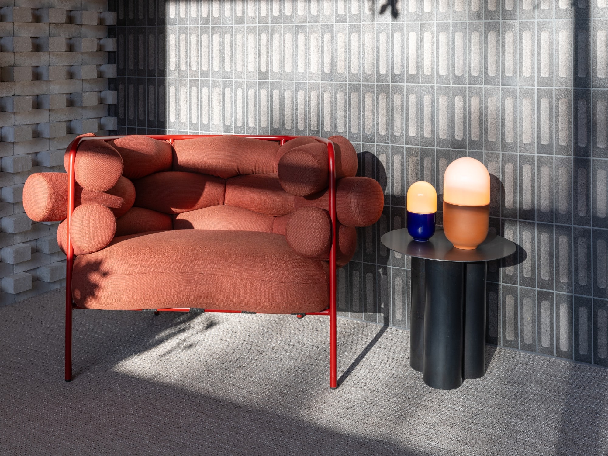 Red modern chair next to a black side table with two lamps in a sunlit room.
