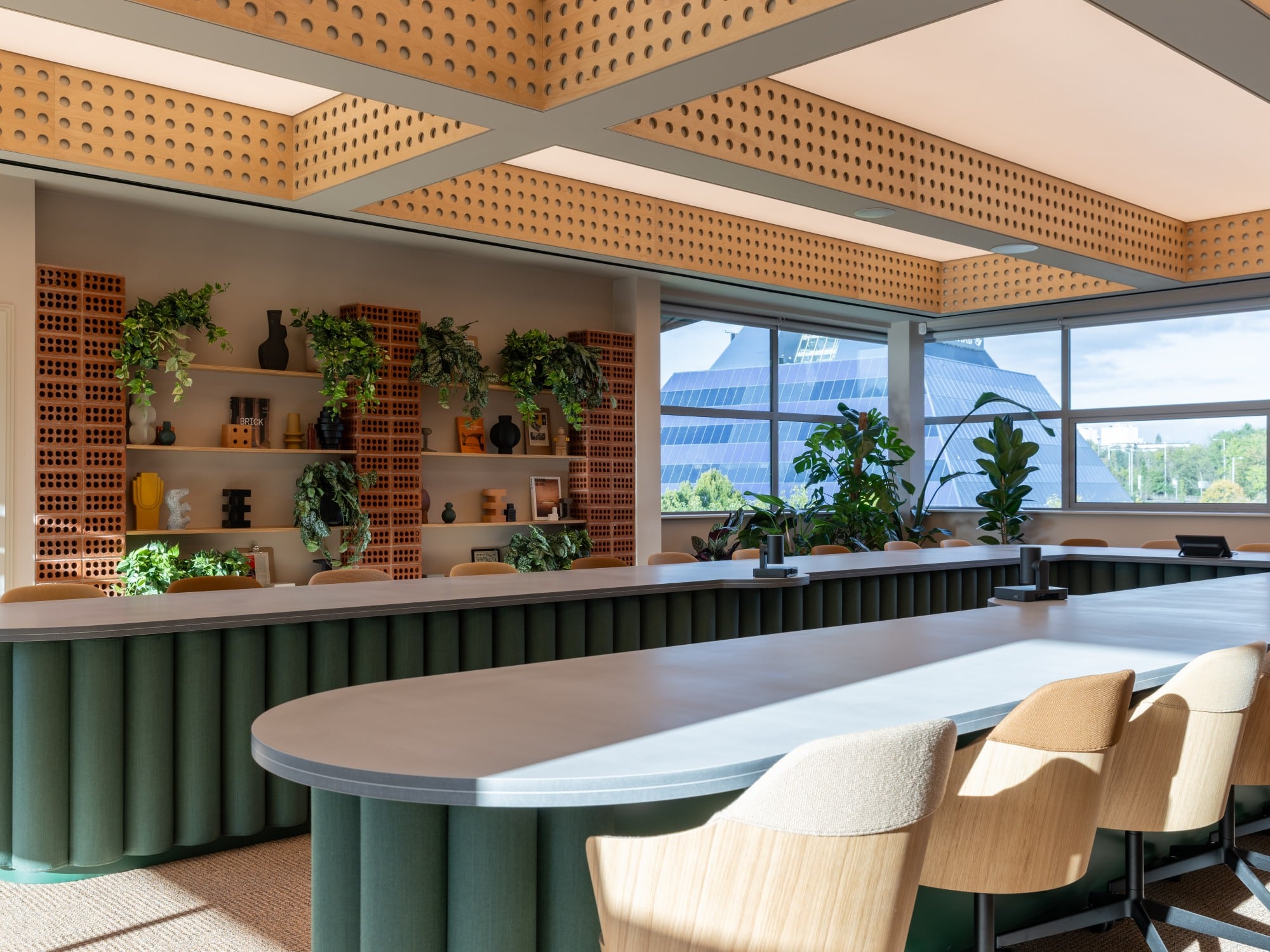 Modern office space with plants, large windows, and a long table with chairs.