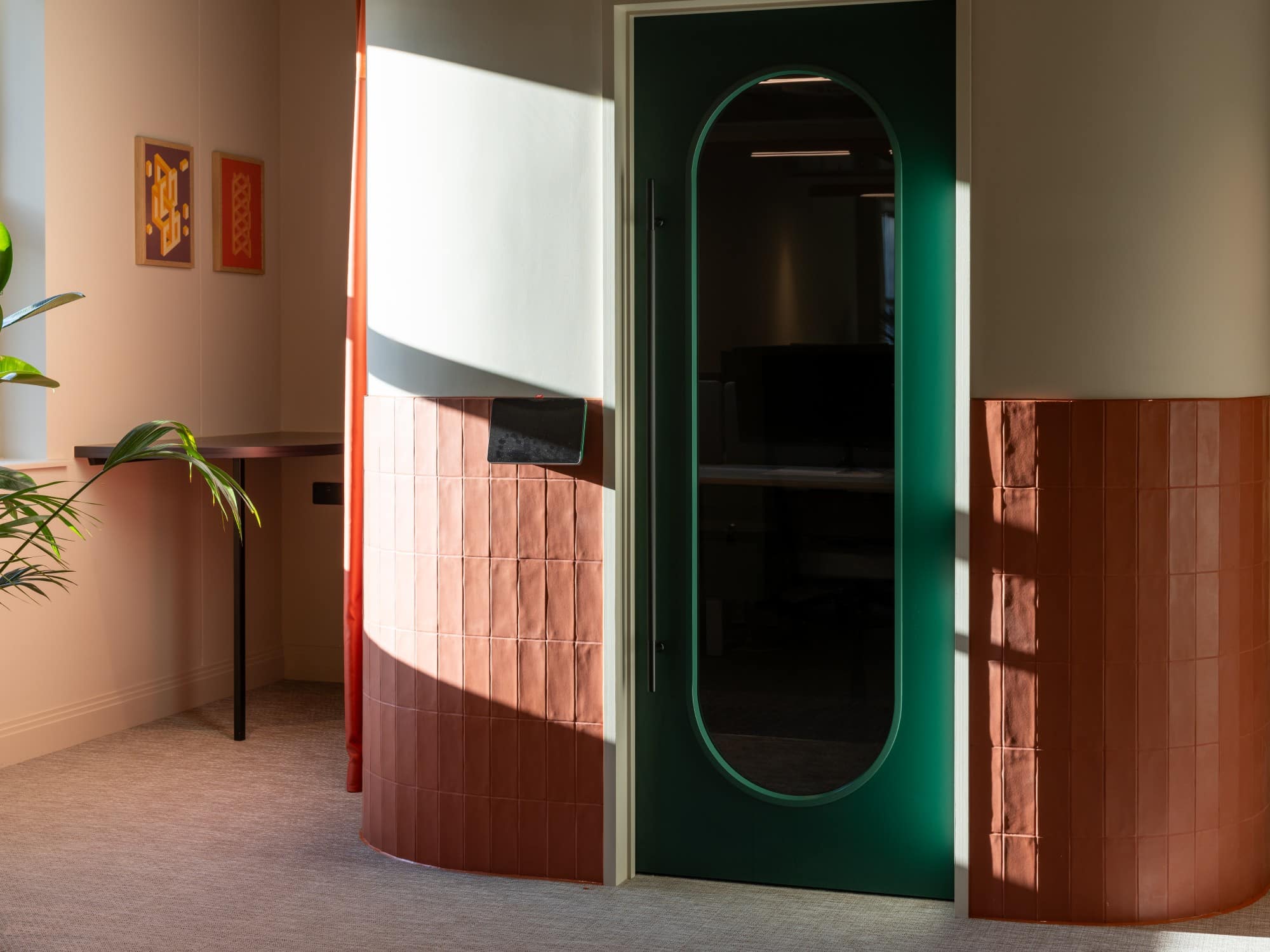 A green door with an oval window in a sunlit room with red and cream walls.